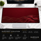Burgundy Evolution desk mat beneath a monitor on a bright desk with a white keyboard and mouse.