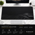 Graphite Evolution desk mat beneath a monitor on a bright desk with a white keyboard and mouse.