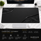 Charcoal Cutaway desk mat beneath a monitor on a bright desk with a white keyboard and mouse.