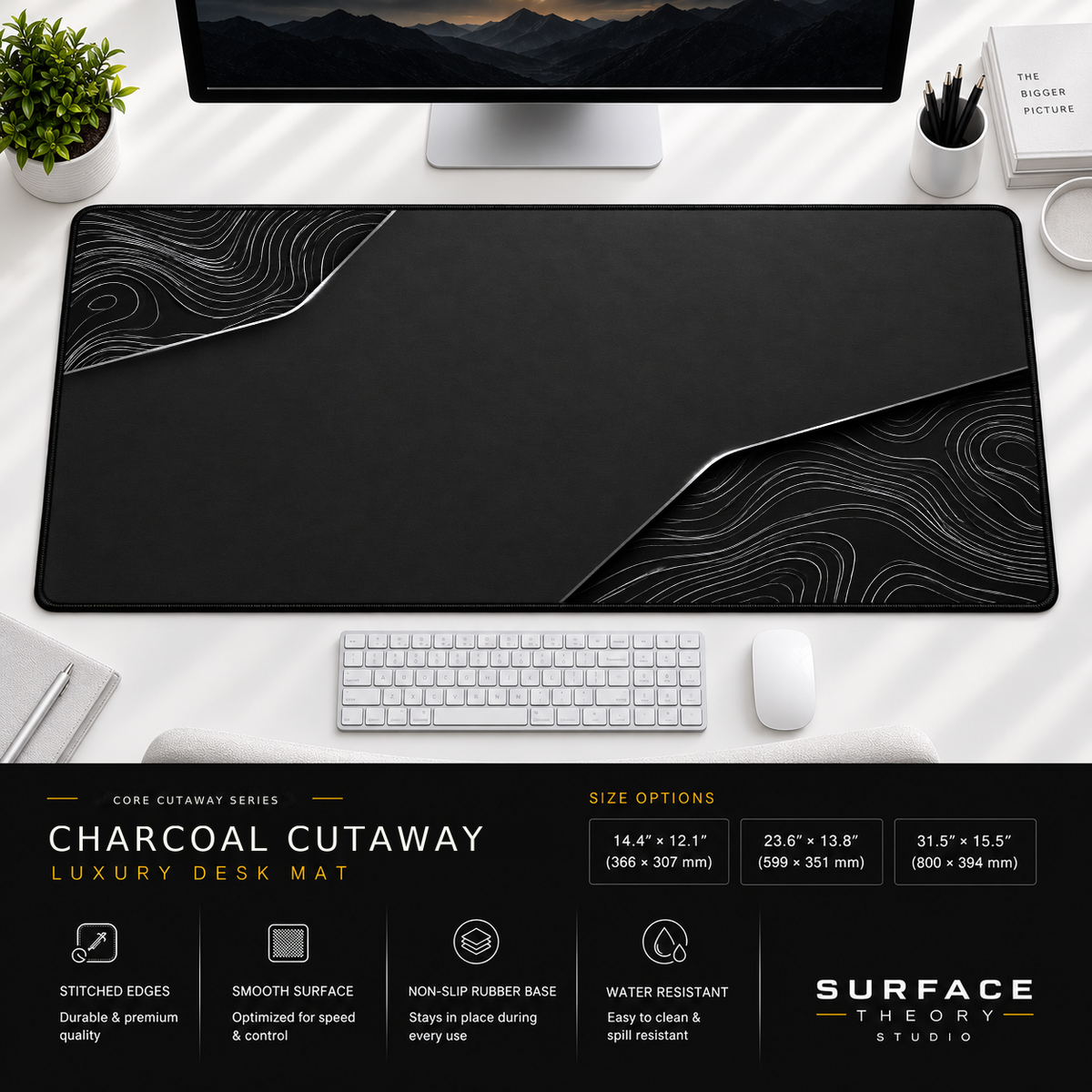 Charcoal Cutaway desk mat beneath a monitor on a bright desk with a white keyboard and mouse.