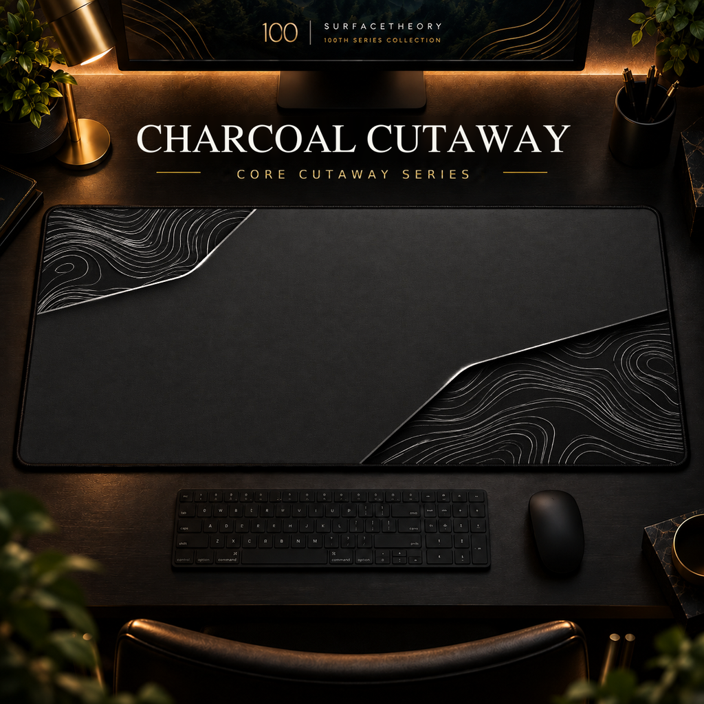 Charcoal Cutaway desk mat, charcoal grey with silver-grey contours in opposing corners, in a warm, dark workspace.
