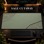 Sage Cutaway desk mat, muted sage green with pale cream-green contours in opposing corners, in a warm, dark workspace.