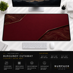 Burgundy Cutaway desk mat beneath a monitor on a bright desk with a white keyboard and mouse.