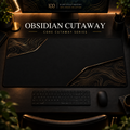 Obsidian Cutaway desk mat, near-black with bronze-gold contours in opposing corners, in a warm, dark workspace.