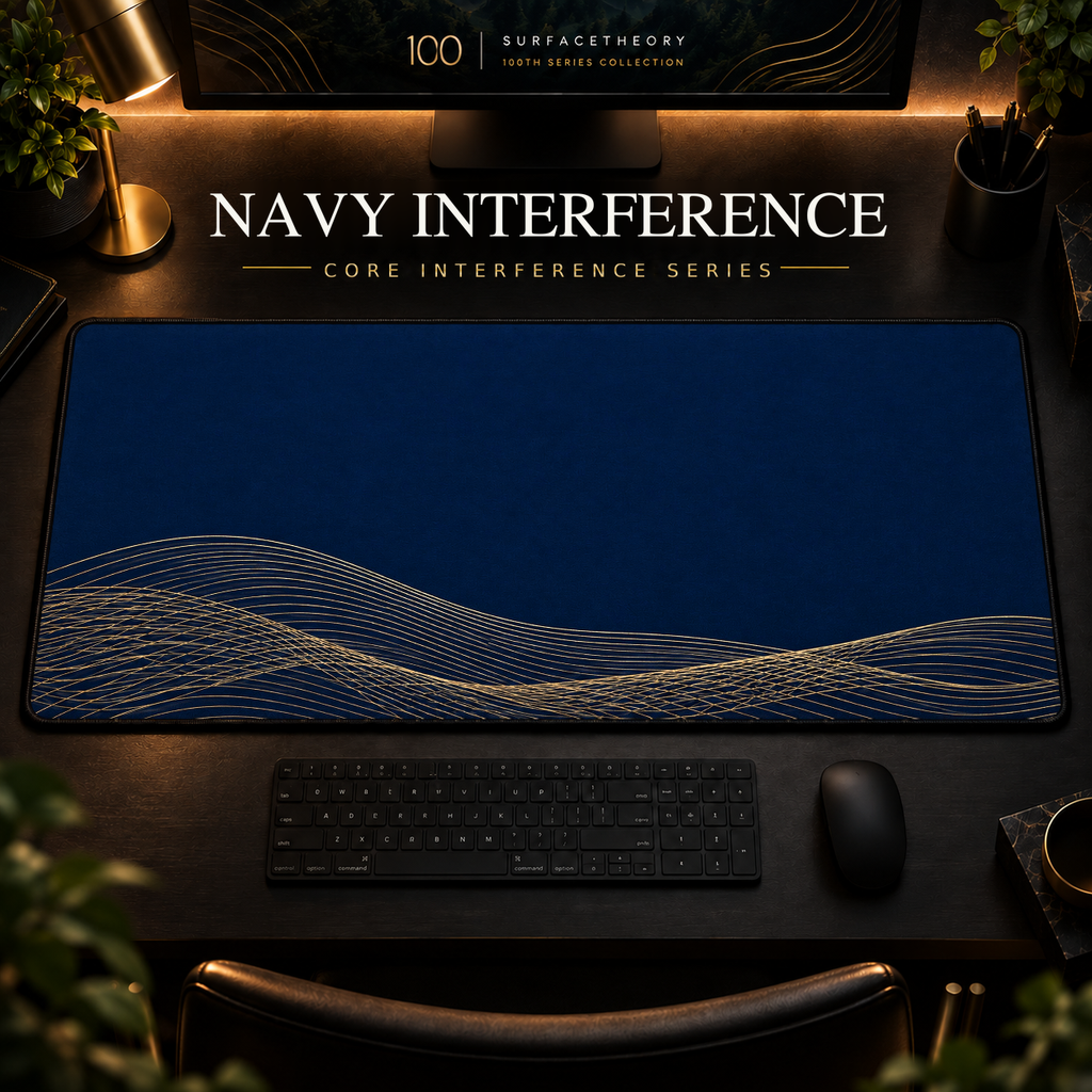 Navy Interference desk mat, navy blue with overlapping gold-toned curves along the lower edge, in a warm, dark workspace.