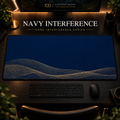 Navy Interference desk mat, navy blue with overlapping gold-toned curves along the lower edge, in a warm, dark workspace.