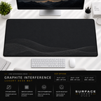 Graphite Interference desk mat beneath a monitor on a bright desk with a white keyboard and mouse.