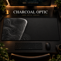 Charcoal Optic desk mat, charcoal grey with silver-grey contours in a rounded form on the left, in a warm, dark workspace.