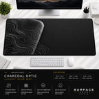 Charcoal Optic desk mat beneath a monitor on a bright desk with a white keyboard and mouse.