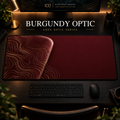 Burgundy Optic desk mat, burgundy with gold-toned contours in a rounded form on the left, in a warm, dark workspace.