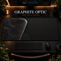 Graphite Optic desk mat, graphite grey with grey contours in a rounded form on the left, in a warm, dark workspace.
