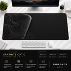 Graphite Optic desk mat beneath a monitor on a bright desk with a white keyboard and mouse.