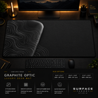 Graphite Optic desk mat in a dark workstation with warm monitor lighting.