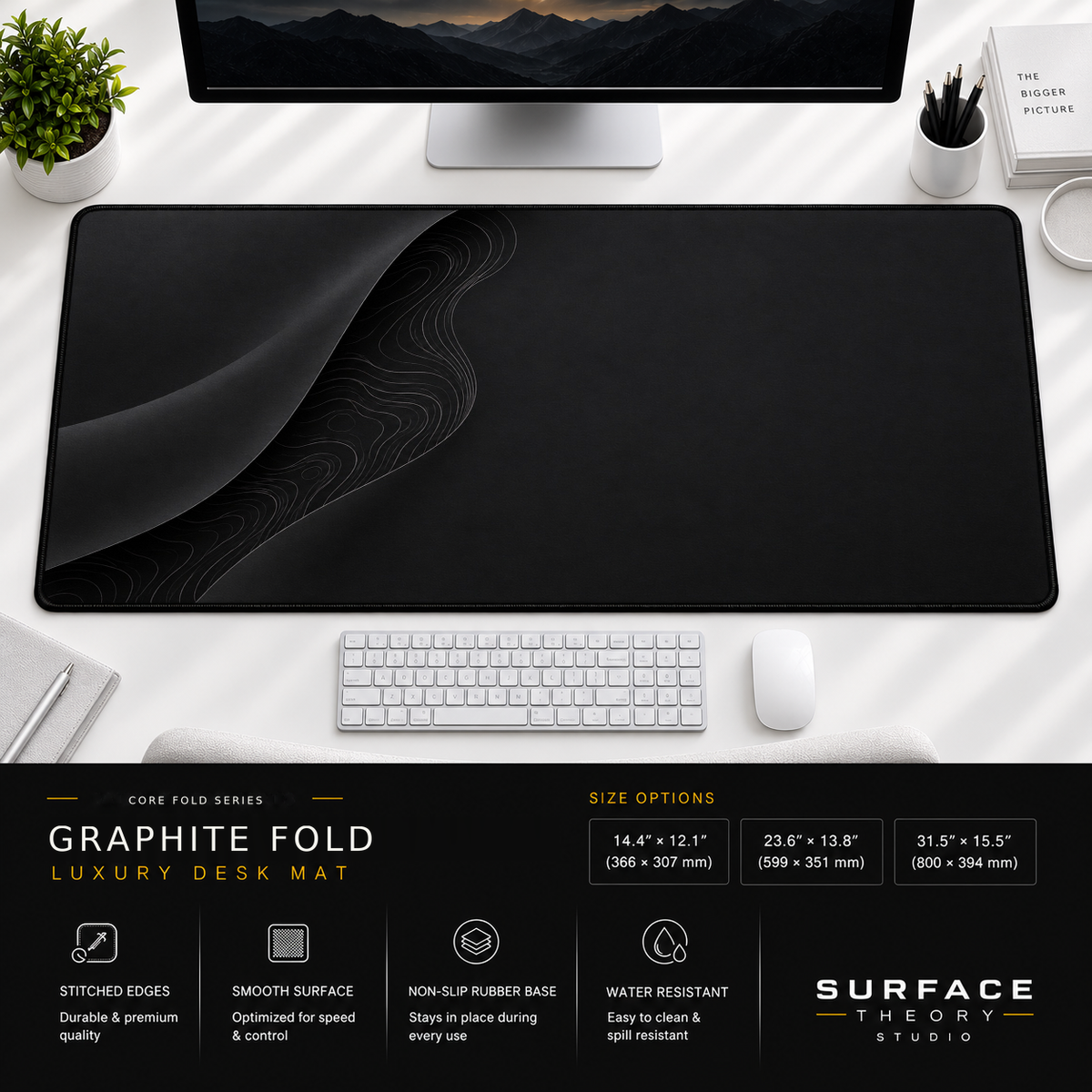Graphite Fold desk mat beneath a monitor on a bright desk with a white keyboard and mouse.