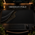 Obsidian Fold desk mat with a sweeping curve and fine contours along the left in a warm, dark workspace.
