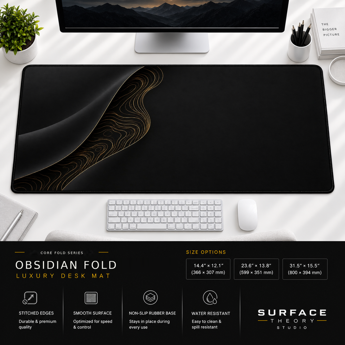 Obsidian Fold desk mat beneath a monitor on a bright desk with a white keyboard and mouse.
