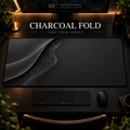 Charcoal Fold desk mat with a sweeping curve and fine contours along the left in a warm, dark workspace.