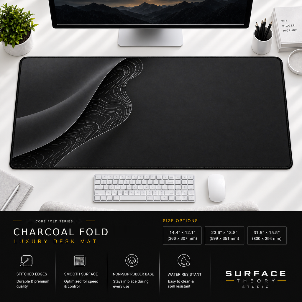 Charcoal Fold desk mat beneath a monitor on a bright desk with a white keyboard and mouse.