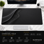 Charcoal Fold desk mat beneath a monitor on a bright desk with a white keyboard and mouse.