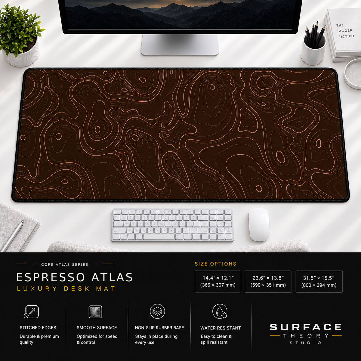 Espresso Atlas desk mat beneath a monitor on a bright desk with a white keyboard and mouse.