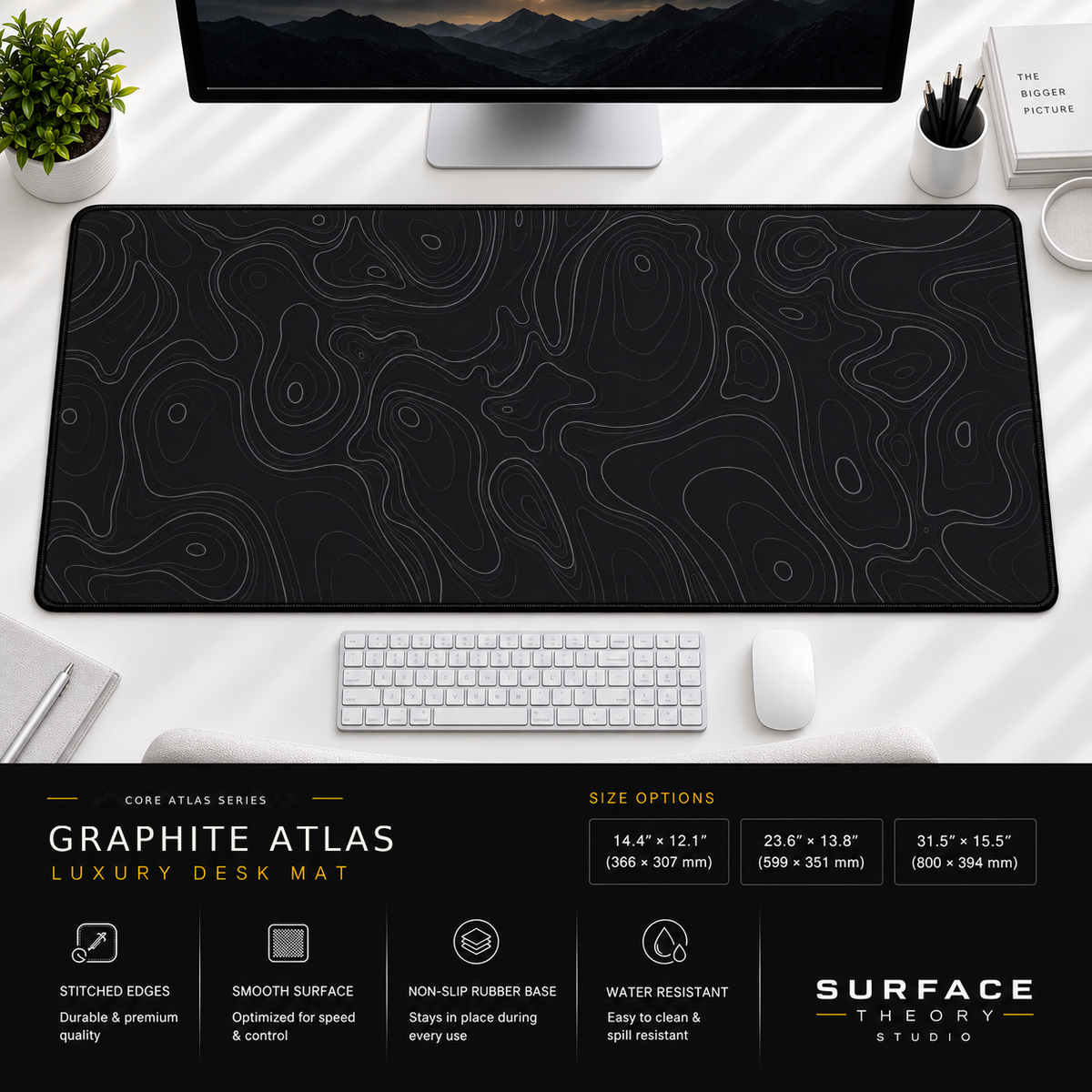 Graphite Atlas desk mat beneath a monitor on a bright desk with a white keyboard and mouse.