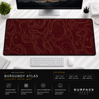 Burgundy Atlas desk mat beneath a monitor on a bright desk with a white keyboard and mouse.