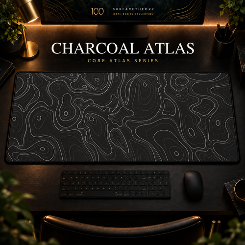 Charcoal Atlas desk mat with fine topographic-inspired contours across the full surface in a warm, dark workspace.