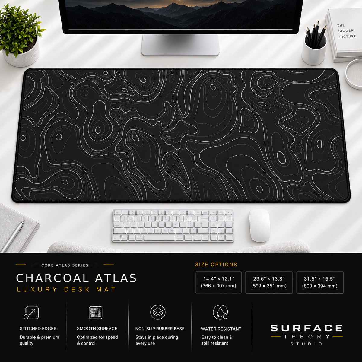 Charcoal Atlas desk mat beneath a monitor on a bright desk with a white keyboard and mouse.