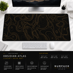 Obsidian Atlas desk mat beneath a monitor on a bright desk with a white keyboard and mouse.