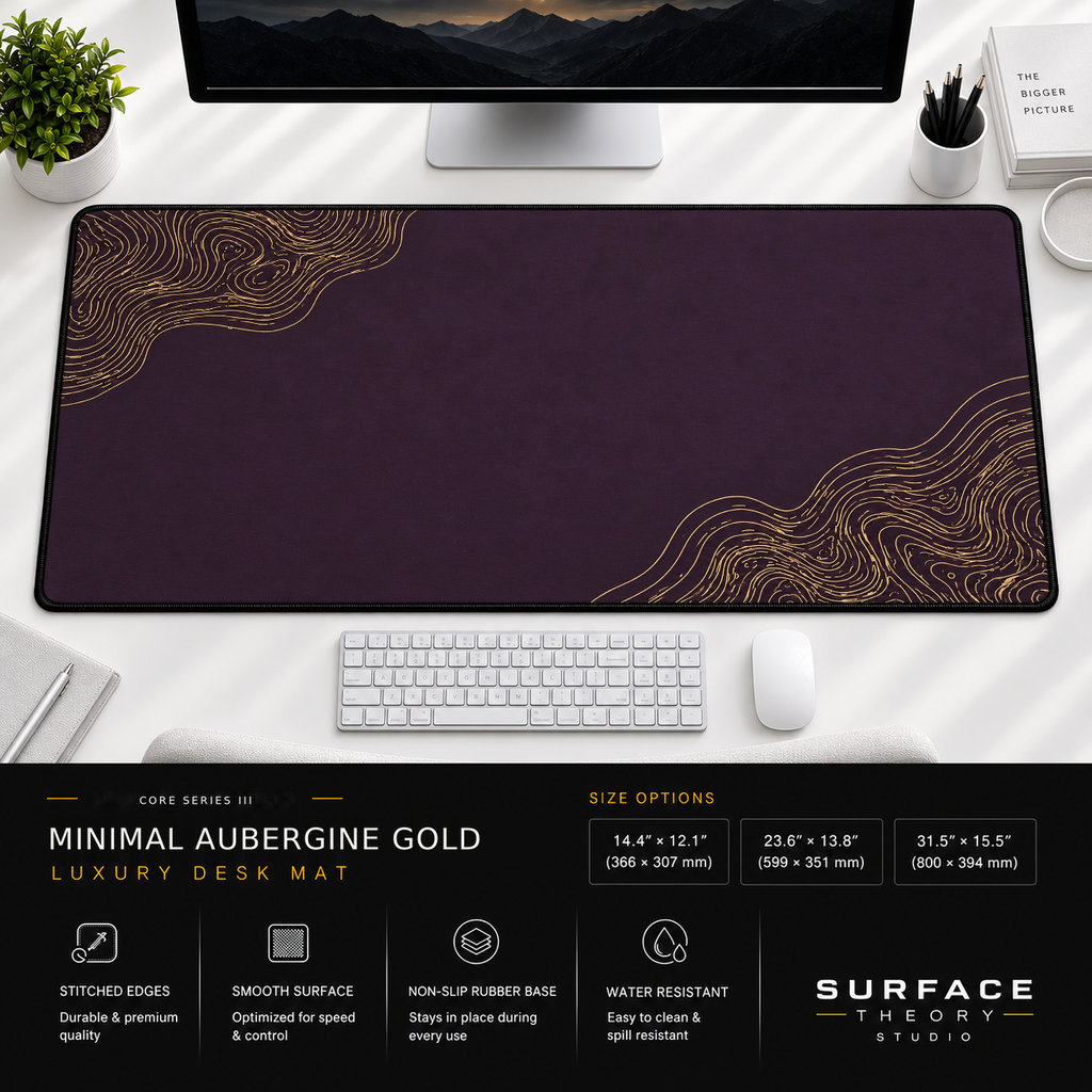 Minimal Aubergine Gold desk mat beneath a monitor on a bright desk with a white keyboard and mouse.