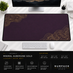 Minimal Aubergine Gold desk mat beneath a monitor on a bright desk with a white keyboard and mouse.
