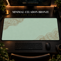 Minimal Celadon Bronze desk mat with fine contours in opposing corners in a warm, dark workspace.