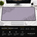 Minimal Smoked Lilac desk mat beneath a monitor on a bright desk with a white keyboard and mouse.