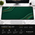 Forest Relief desk mat beneath a monitor on a bright desk with a white keyboard and mouse.