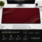 Burgundy Relief desk mat beneath a monitor on a bright desk with a white keyboard and mouse.