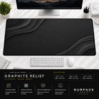 Graphite Relief desk mat beneath a monitor on a bright desk with a white keyboard and mouse.