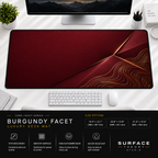Burgundy Facet desk mat beneath a monitor on a bright desk with a white keyboard and mouse.