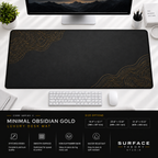 Minimal Obsidian Gold desk mat beneath a monitor on a bright desk with a white keyboard and mouse.