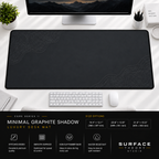 Minimal Graphite Shadow desk mat beneath a monitor on a bright desk with a white keyboard and mouse.