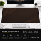 Minimal Espresso Bronze desk mat beneath a monitor on a bright desk with a white keyboard and mouse.