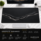 Graphite Radiance desk mat beneath a monitor on a bright desk with a white keyboard and mouse.